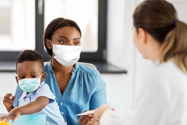 Doctor talking to mother with baby son wearing protective medical mask at clinic