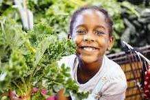 Child smiling next to leaf lettuce plant