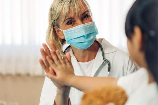 Woman doctor wearing protective mask talking to little girl patient