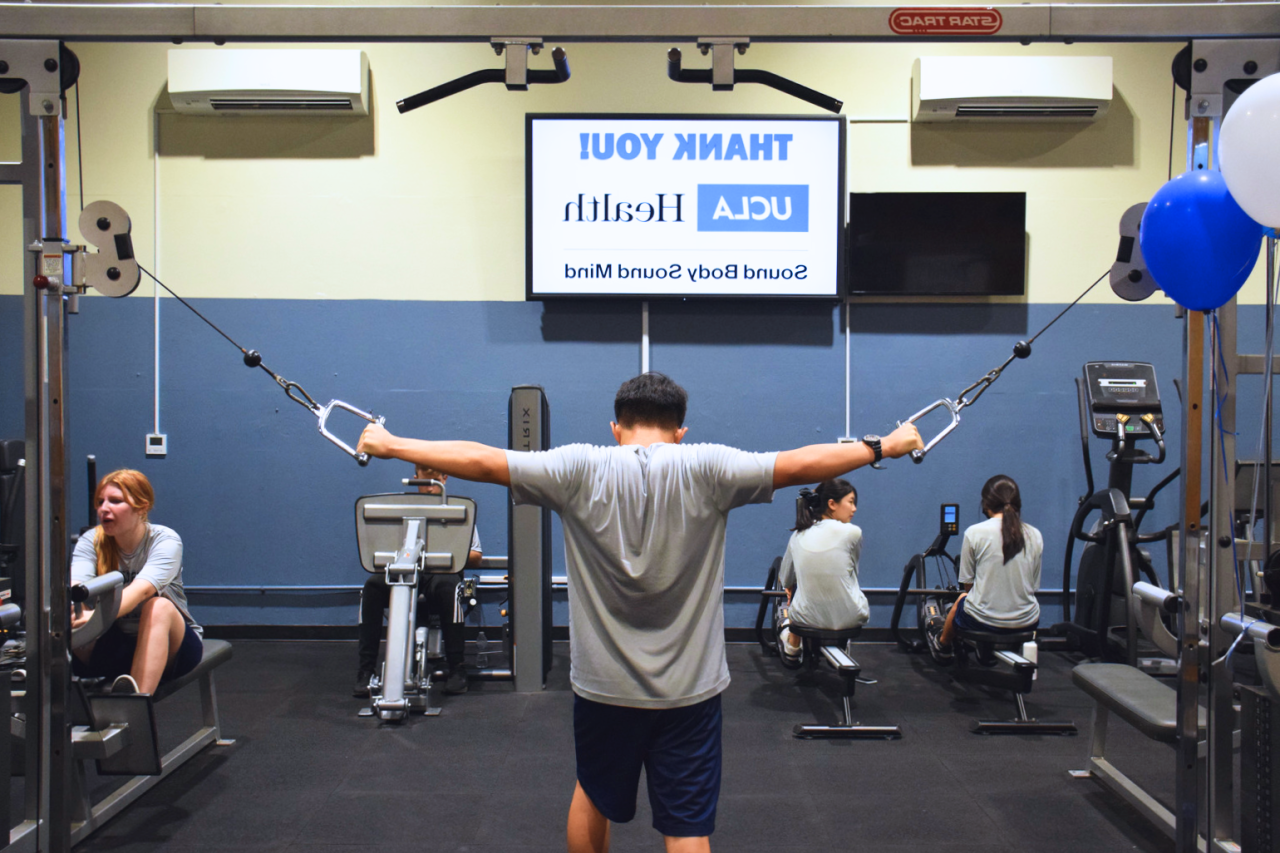 Student in PE class performs exercise. "Thank you UCLA Health Sound Body Sound Mind" is projected on a screen in the background.